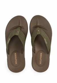 Brune gummiflip-flops med grønne vævede stropper, der har et rundt logo og et lille accentmærke. Tekstureret hæl for greb og komfort.