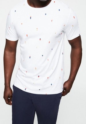 Valkoinen lyhythihainen t-paita, jossa on hajautettu kuvio pieniä punaisia, keltaisia ja sinisiä täpliä. Pehmeä kangas, pyöreä pääntie, rento istuvuus.