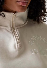 Il pullover beige a mezza zip presenta la scritta ricamata "DODGERS" e "1944" in filo chiaro. Tessuto morbido con una texture liscia e colletto aderente.