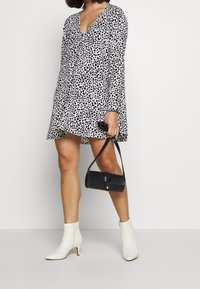 Černobíle skvrnité šaty s dlouhými rukávy a výstřihem do V, doplněné o bílé kotníkové boty a malou černou kabelku.