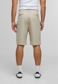 Beige shorts van gladde stof, met een regular fit, twee achterzakken en een nette zoom, gecombineerd met witte sokken en schoenen met zwarte accenten.