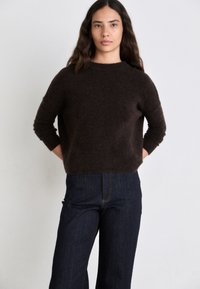 Brown knit sweater with a round neckline and long sleeves, paired with dark blue high-waisted jeans, set against a neutral backdrop.
