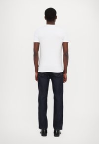 Hvid kortærmet t-shirt parret med mørkeblå lige ben jeans. Glat tekstur med synlige sømme og en baglomme detalje.