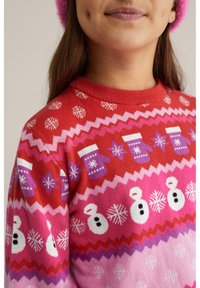 Sarkana un rozā adīta džemperis ar sniegavīriem, cimdiem un sniega lāseļiem zigzagā rakstā; mīksta tekstūra ar apaļu izgriezumu.