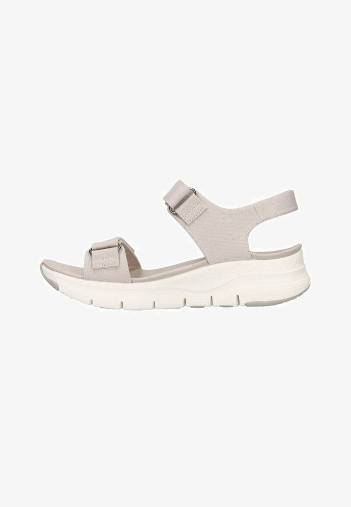 Sandalias deportivas de color beige claro con una correa elástica y hebillas ajustables. Suela acolchada con detalles texturizados y un diseño ligero.