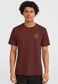 Bordeaux katoenen t-shirt met korte mouwen, ronde hals en een cirkelvormige patch met een ontwerp in oranje op de linkerkant van de borst.