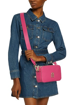 Kleine rosa Leder-Schultertasche mit texturiertem Finish, einem metallischen Logo-Akzent und einem abnehmbaren breiten Tragegurt, kombiniert mit einem Denim-Kleid.