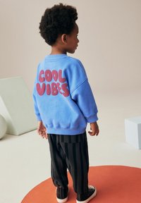 Sweatshirt bleu clair avec "COOL VIBES" en lettres rose foncé, associé à un pantalon rayé noir et des baskets noires.