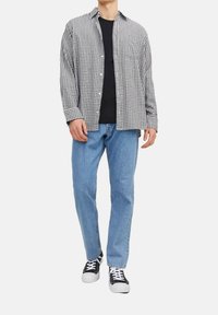 Zwart-wit geblokt shirt, lange mouwen, met knopen, gedragen over een zwart shirt. Lichtblauwe spijkerbroek, casual zwarte sneakers met een witte zool.