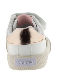 Baskets blanches avec une languette arrière en métal rose doré, doublure intérieure rose, bande auto-agrippante et semelle texturée beige portant l'étiquette "victoria" à l'arrière.