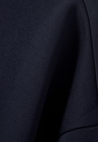 Tessuto blu navy con una superficie liscia e texture. Il materiale sembra leggermente elastico, adatto per abbigliamento casual o uso attivo.