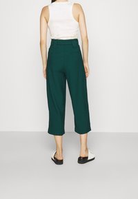 Gröna capribyxor med hög midja och vida ben, tillverkade av lätt tyg; åks med en vit ärmlös topp och platta sandaler.