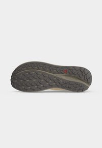 Semelle d'une chaussure de plein air gris foncé avec motif de semelle texturé et petit logo triangulaire rouge près du centre, sur un fond clair uni.