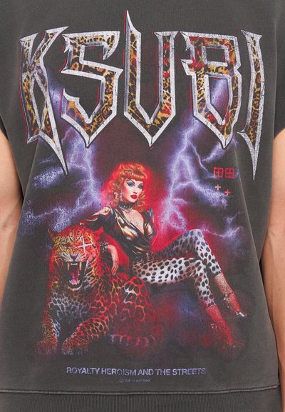 T-shirt graphique noir avec des lettres "KSUBI" en gras, une œuvre colorée représentant une figure aux cheveux rouges et des léopards, le tout avec un fond de foudre.