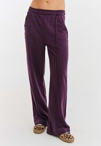 Fialové, volné tepláky vyrobené z měkk�ého materiálu, s elastickým pasem a dvěma bočními kapsami. V páru s pantoflemi s leopardím potiskem.