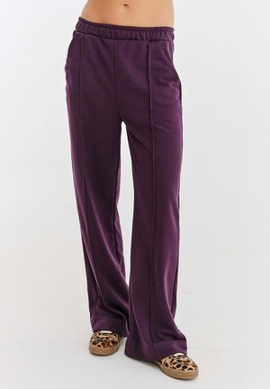 Fioletowe, luźne spodnie dresowe z miękkiego materiału, z elastycznym paskiem w talii i dwoma bocznymi kieszeniami. Połączone z kapciami w panterkę.