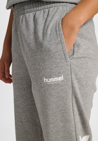 Grå joggerbyxor i mjukt material med elastisk midja och sidofickor, med en liten vit logotyp tryckt på framsidan.