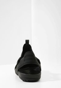 Sandal negro de cierre trasero con un upper texturizado, una correa acolchada y una suela de goma. Diseño minimalista con una lengüeta trasera para poner y quitar fácilmente.