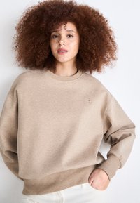Beige genser med rund hals, ribbestrikkede mansjetter og hem, med en subtil logo på brystet. Mykt stoff, avslappet passform og medium lengde.
