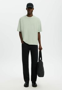 T-shirt oversize vert clair, jeans noirs à jambes droites, casquette noire, sac noir avec bandoulières, chaussures noires. Vêtements simples et confortables à coupe décontractée.