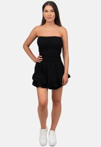 Zwarte, strapless jurk met een gerimpelde buste en een gerimpelde zoom. Draag met witte sneakers. Gladde textuur en lichtgewicht stof.