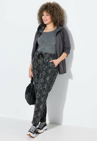 Pantalons de survêtement à motifs noir et blanc avec une taille élastique, un débardeur gris chiné et une veste zippée grise assortie. Sac noir et baskets.