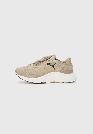 Beżowy dziergany sneaker Puma z grubą białą podeszwą, beżowymi sznurowadłami i czarnym logo Puma po boku, pokazany w widoku z profilu.