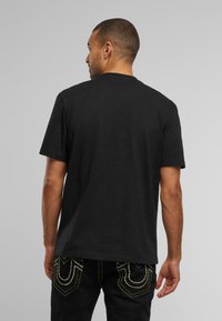 Zwarte katoenen T-shirt met korte mouwen en een klassieke ronde hals, gedragen met een donkere jeans met contrasterende gele stiksels op de zakken.