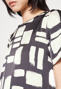 Blusa de manga corta en negro y crema, con un patrón de pinceladas y formas rectangulares. Fabricada en una tela suave y ligera.