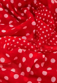 Tessuto rosso con una texture morbida e trasparente, caratterizzato da grandi pois bianchi sparsi. Il materiale appare leggero e fluido.