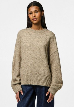 Maglione beige lavorato a maglia con scollo a girocollo, spalle scese e polsini e orlo a coste. Indossato sopra jeans blu a gamba larga, caratterizzati da un motivo testurizzato.