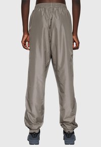 Grå syntetiska träningsbyxor med elastisk midja och muddar, med en slät yta och avslappnad passform. Skor syns i botten.