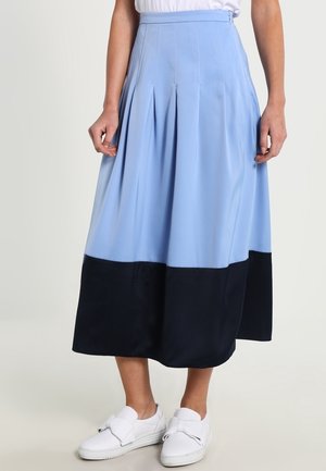 Gonna midi azzurra chiara con ampio orlo nero indossata con sneakers bianche slip-on, mostrata dalla vita ai piedi su sfondo neutro.
