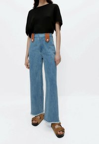 Lyseblå vidde jeans med læderdetaljer og trykknapper, kombineret med en sort ribbet t-shirt og brune platformsandaler.