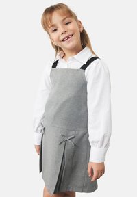 Grå klänning av tyg med svarta remmar, som har veck och rosettdetaljer på sidorna. Vit långärmad skjorta under synlig.