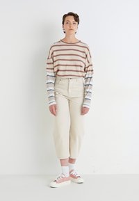 Stripet langermet topp i beige, brun og blå, kombinert med høyt midje korte jeans i elfenben og rosa og hvite sneakers.