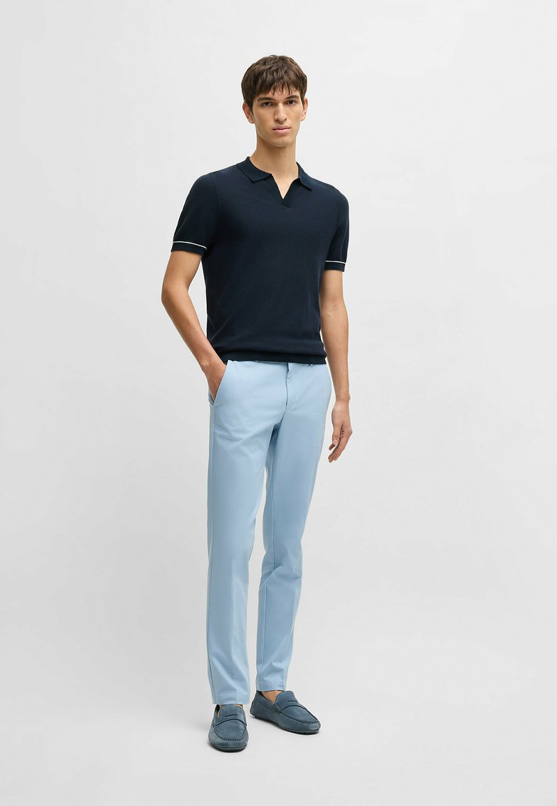 Marineblå polo skjorte med korte ærmer og V-udskæring, parret med lyseblå slim-fit bukser og marineblå loafers.