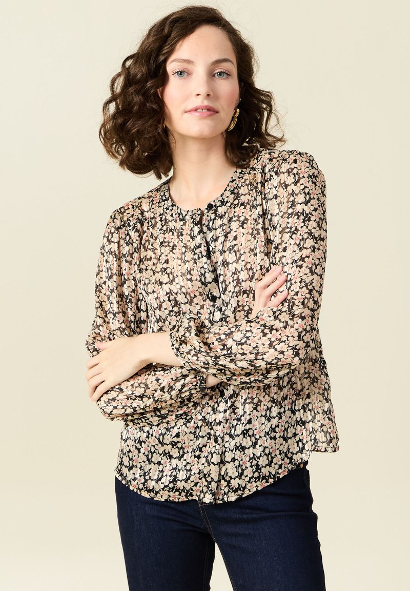 Blusa floreale in morbido tessuto nero trasparente, con scollatura rotonda, chiusura a bottone e maniche a sbuffo con polsini elastici. Motivo floreale scuro su tutta la superficie.