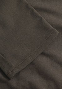 Donkerbruin ribbelstof met een gladde textuur; heeft een omgeslagen rand en subtiele stikdetails. Geschikt voor casual dragen of om te lagen.