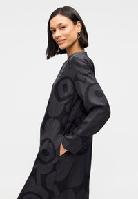 Μαύρο φόρεμα με φλοράλ σχέδιο σε σκούρες αποχρώσεις, μακριά μανίκια και στρογγυλή λαιμόκοψη. Το ύφασμα έχει λεία, υφήμένη επιφάνεια.