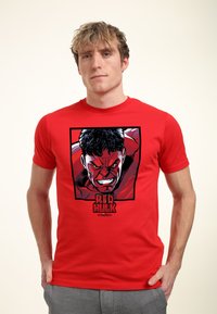 Rød bomulds T-shirt med grafik af karakteren Red Hulk, med iøjnefaldende farver og sort kant, anbragt inden for et sort rektangel.