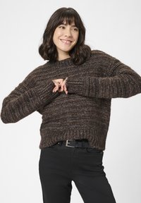 Barna kötött pulóver bordázott mintával, széles ujjakkal és kerek nyakkivágással, fekete nadrággal és övvel párosítva.