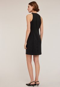 Svart ärmlös klänning med en åtsittande silhuett, slät textur och sömdetaljer bak. Matchas med svarta slingbacks.
