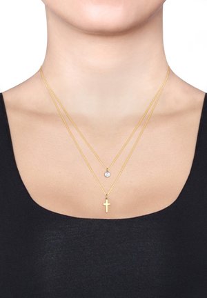 Halskette mit drei Strängen in Goldoptik, die ein kleines Kreuz-Anhänger, einen runden Stein-Anhänger und feine Kettenglieder zeigt. Strukturierte Oberfläche und glatte Akzente.