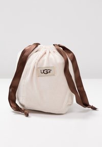 Petit pochon en velours côtelé blanc avec cordon de serrage, rubans de satin marron et patch logo UGG cousu à l'avant.