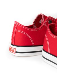 Red canvas sneakers with white sole, black stripe, and contrasting white stitching. Features logo detail on the heel and round eyelets.