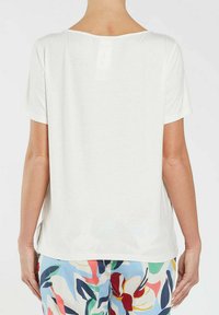 Hvid kortærmet bluse med løs pasform, featuring en rund halsudskæring og sideslids. Glat stoftekstur, falmet mærke synligt på ryggen.