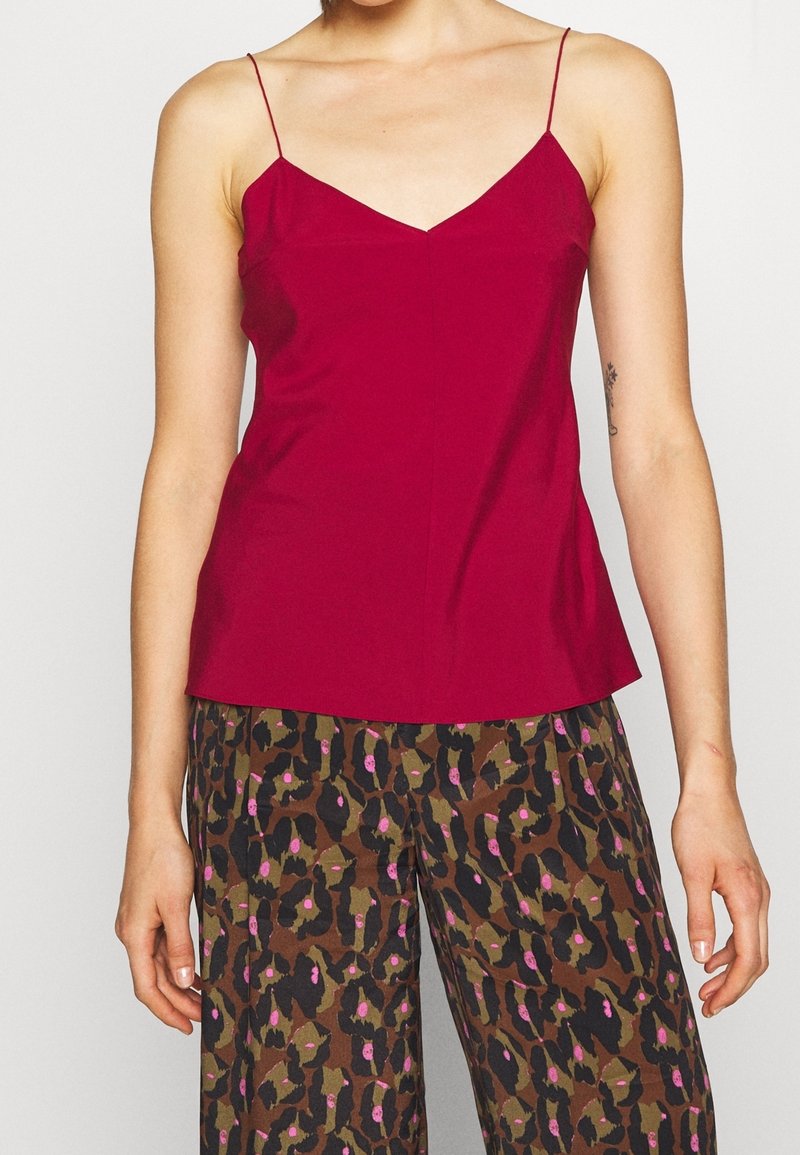 Femme portant un caraco rouge sans manches à fines bretelles et un pantalon ample à motifs floraux abstraits marron, noir et rose.