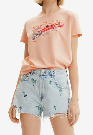 Brzoskwiniowa koszulka z czerwonym samochodem i napisem „Let's Take A Ride” zestawiona z jasnymi dżinsowymi szortami z haftem przedstawiającym małe palmy i ananasy.
