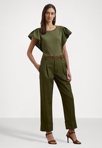 Blusa verde de manga curta com ombros franzidos, combinada com calças verdes de cintura alta e pregas. Cinto castanho com fivela metálica circular. Sandálias de salto bejes.